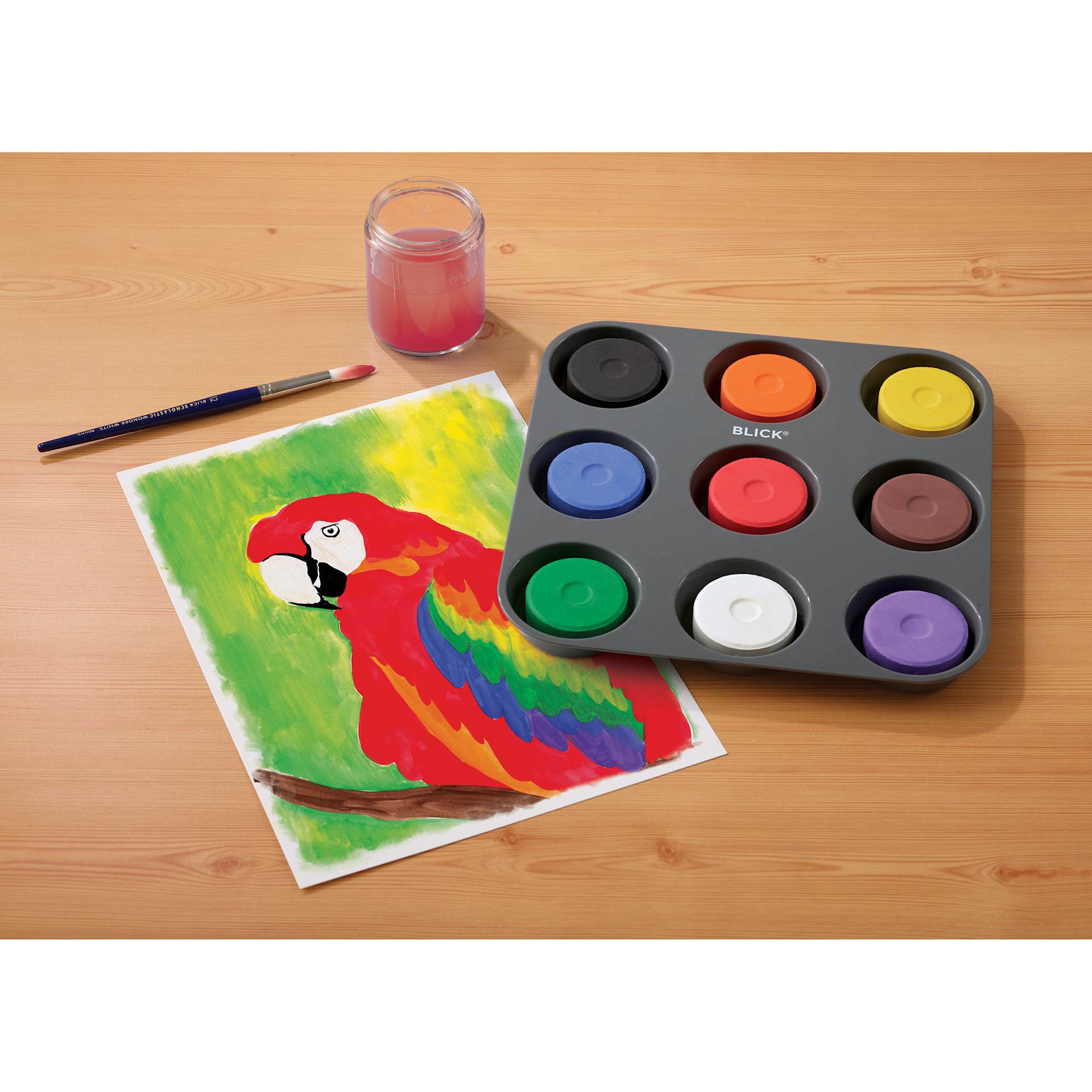Blick Essentials Tempera Cakes Set of 9 Classic Colors in a tray, with brushes, a water cup, and a painting of a parrot.