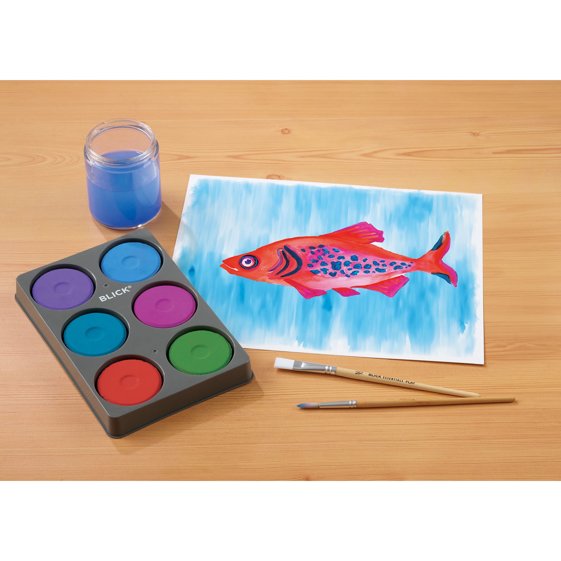 Blick Essentials Tempera Cakes Set of 6 Secondary Colors in a Tray, with brushes, a cup of water, and a painting of a fish.
