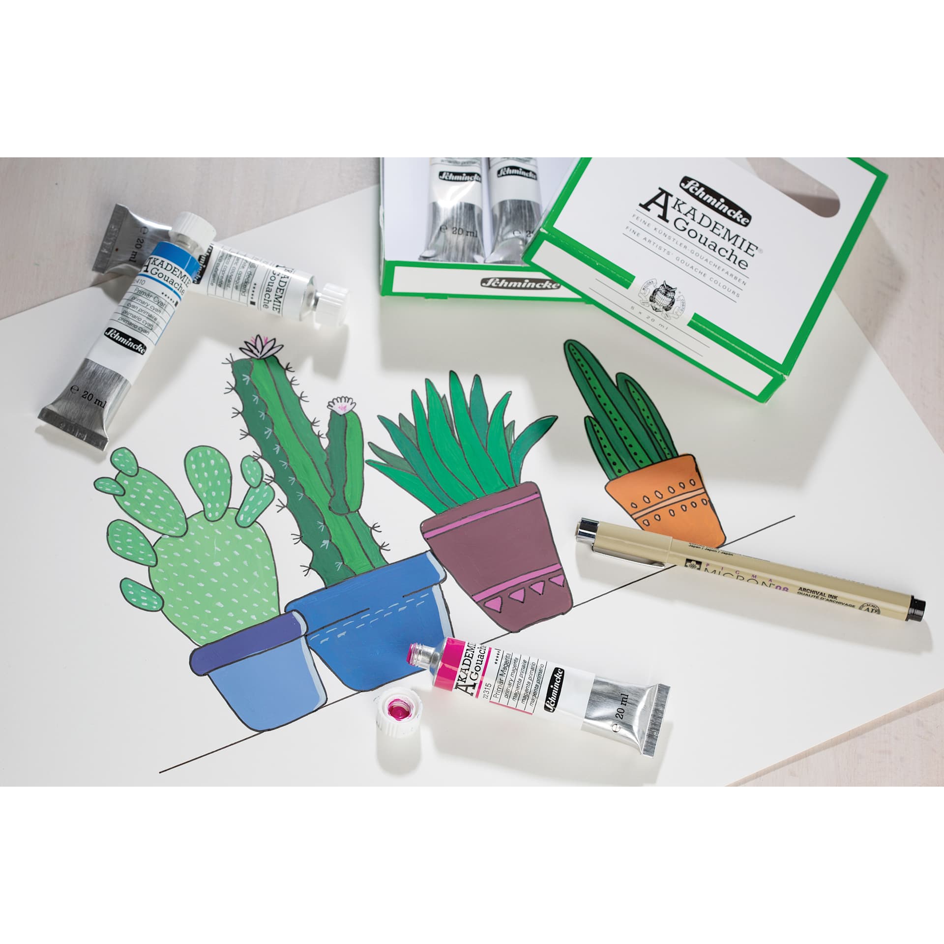 Schmincke Akademie CMYK Starter Gouache Paints laying beside cactus painting