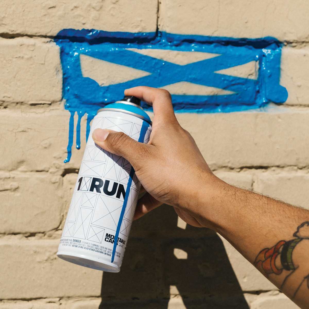 Montana 1XRUN Limited Edition Spray Paint - Blue Magic, 400 ml (Artist spraying paint on brick wall)