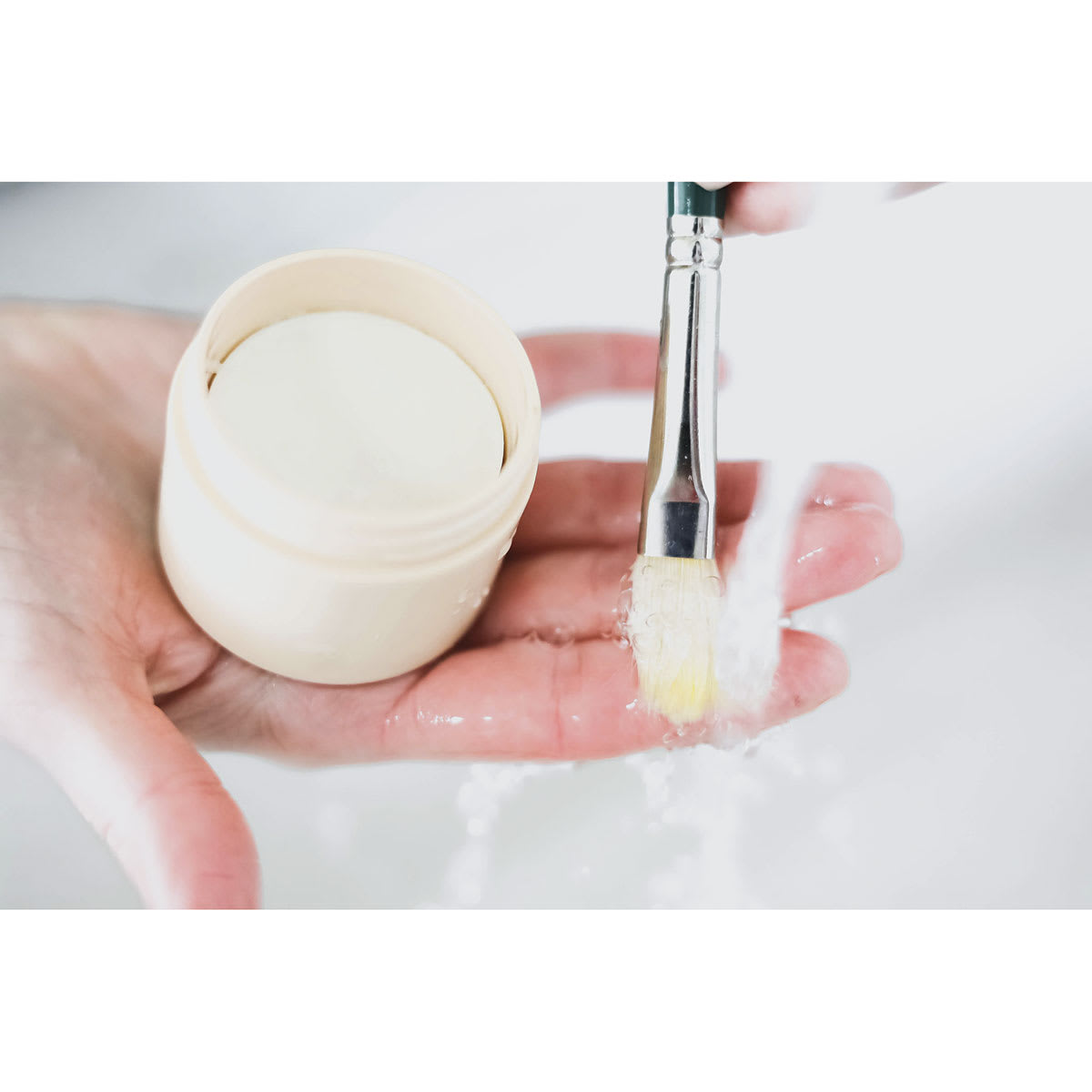 The Masters Brush Cleaner and Preserver - Tub and brush in palm with water running over bristles.