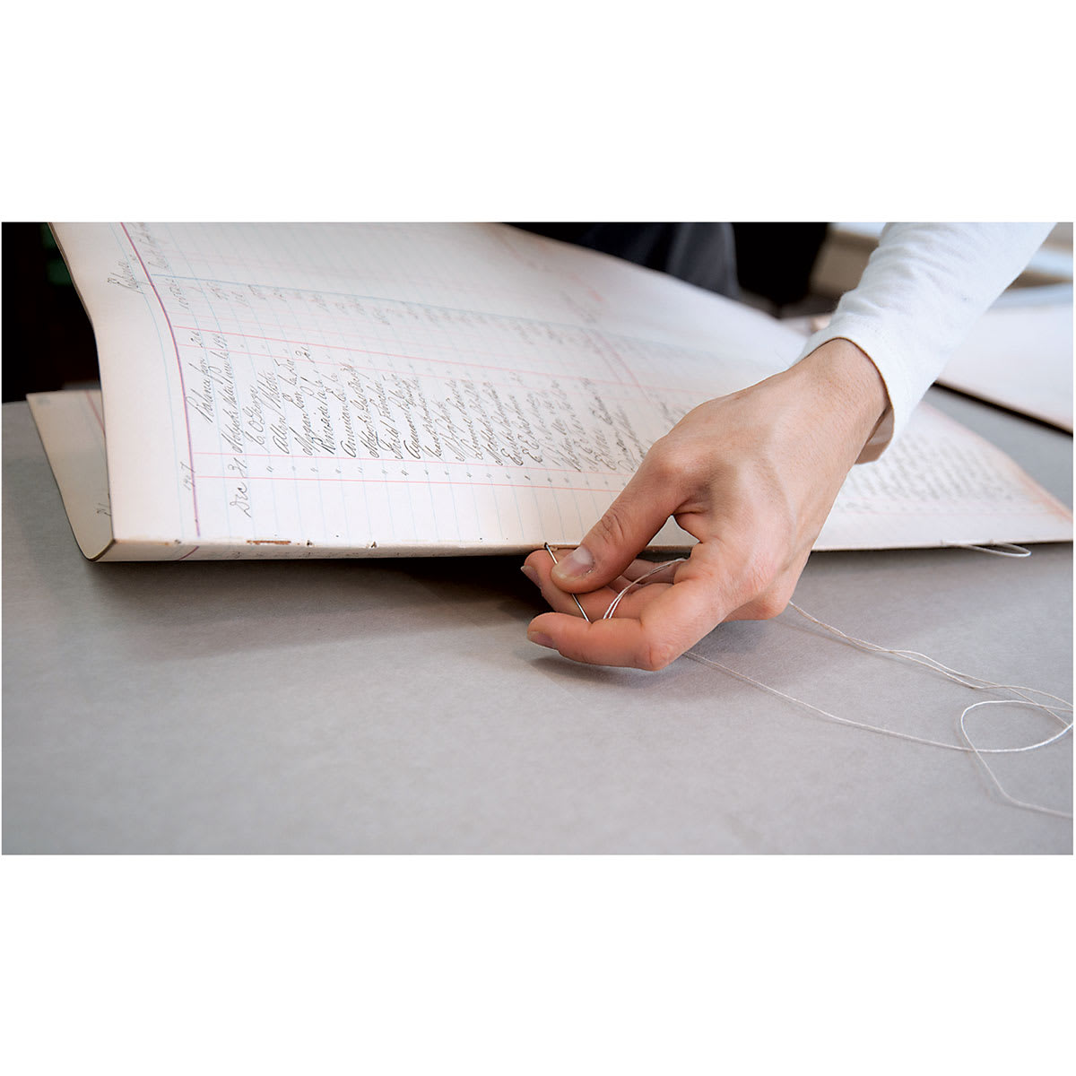 Closeup of hand using Lineco Binder's Needle to bind Ledger pages together