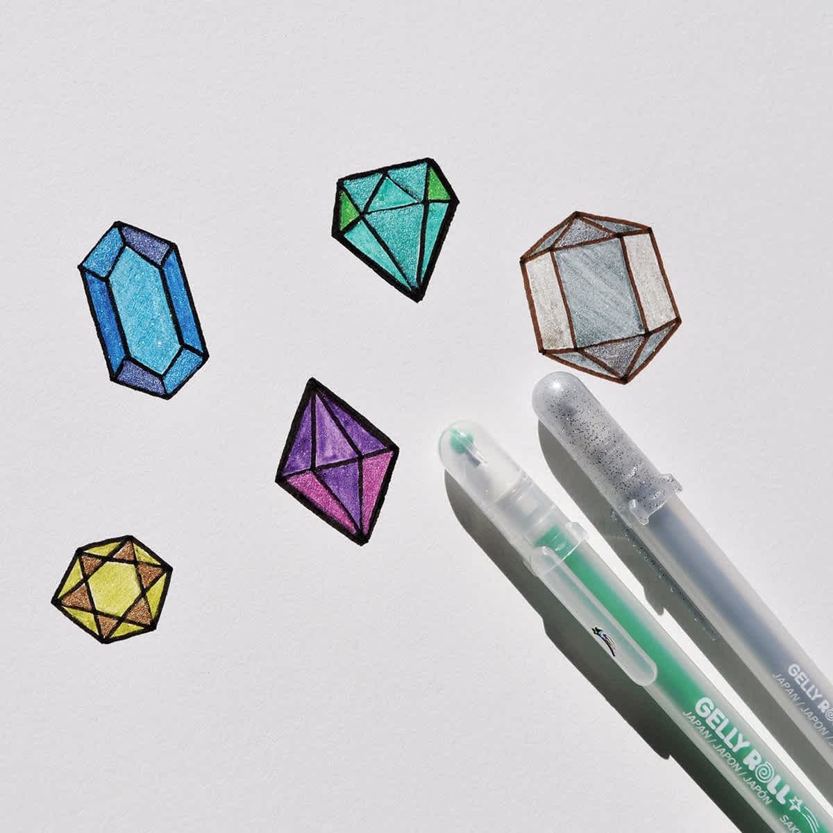 Sakura Gelly Roll Stardust Pens  - 2 Pens lying on a drawing of gemstones