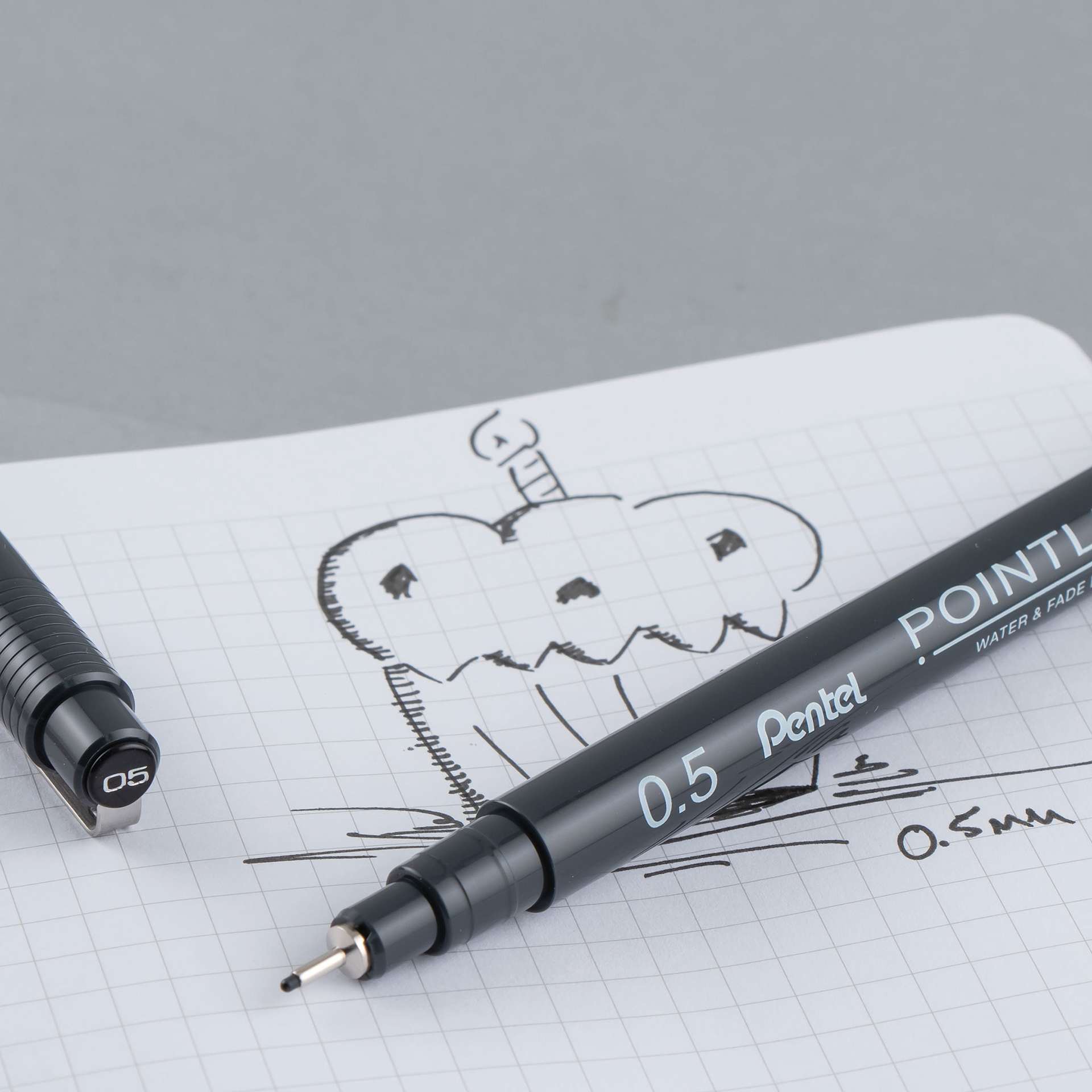 Pentel Arts Pointliner Pen - Uncapped Black pen with sketch of cupcake on graph paper