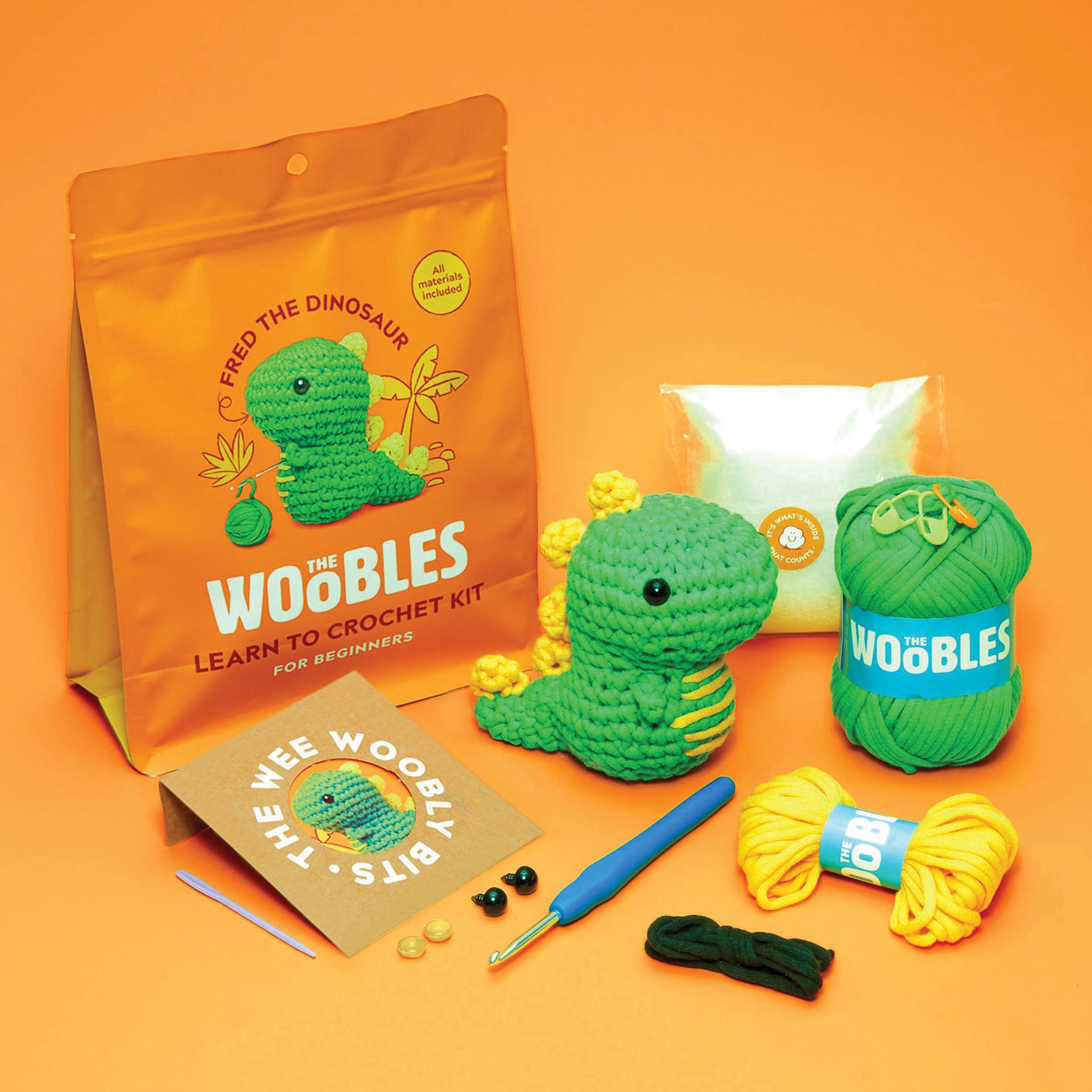 The Woobles Beginner Crochet Amigurumi Kit - Dinosaur, finihsed design and contents laid out in front of packaging