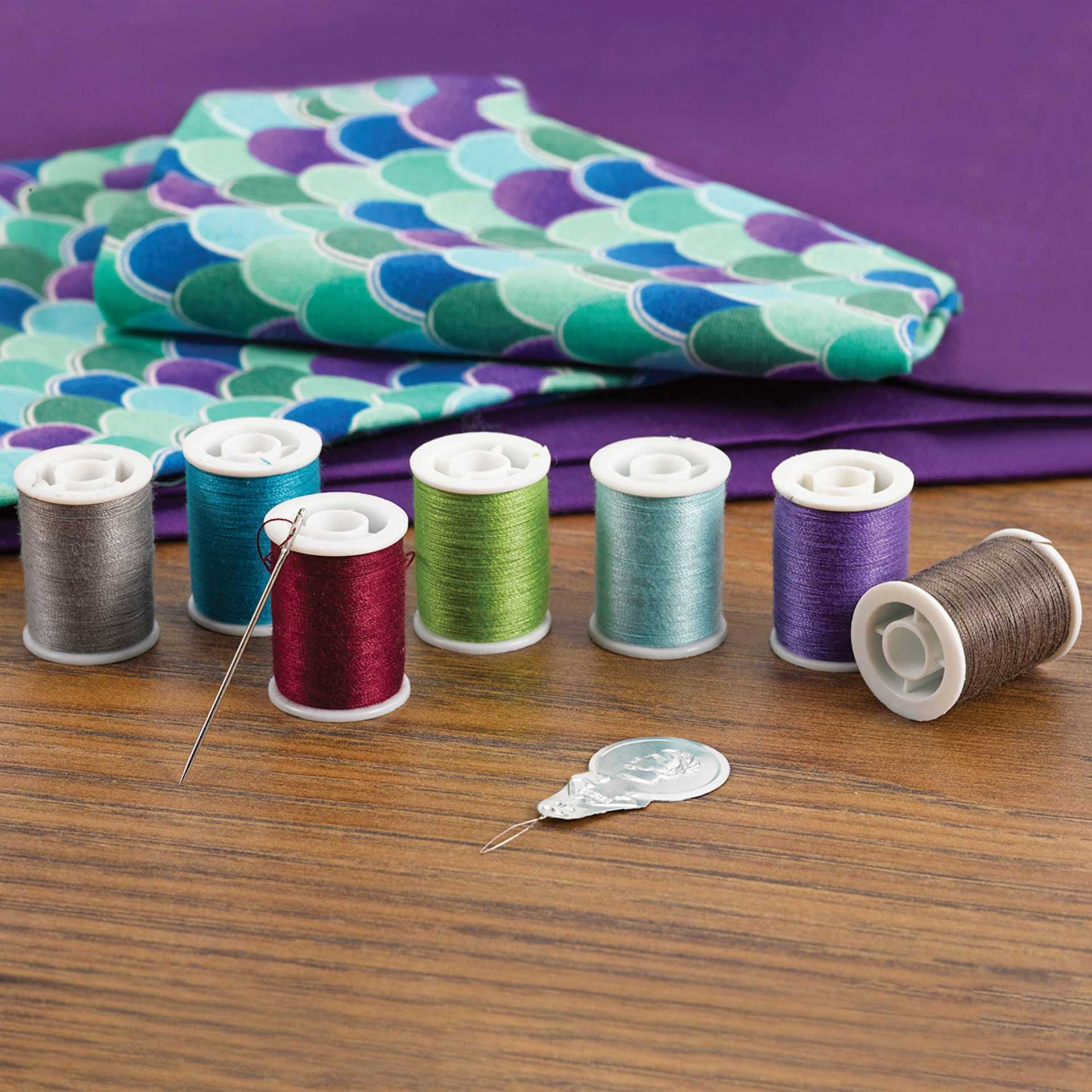 Singer All Purpose Sewing Thread Set - assortment of spools, needle, and needle threader near fabric