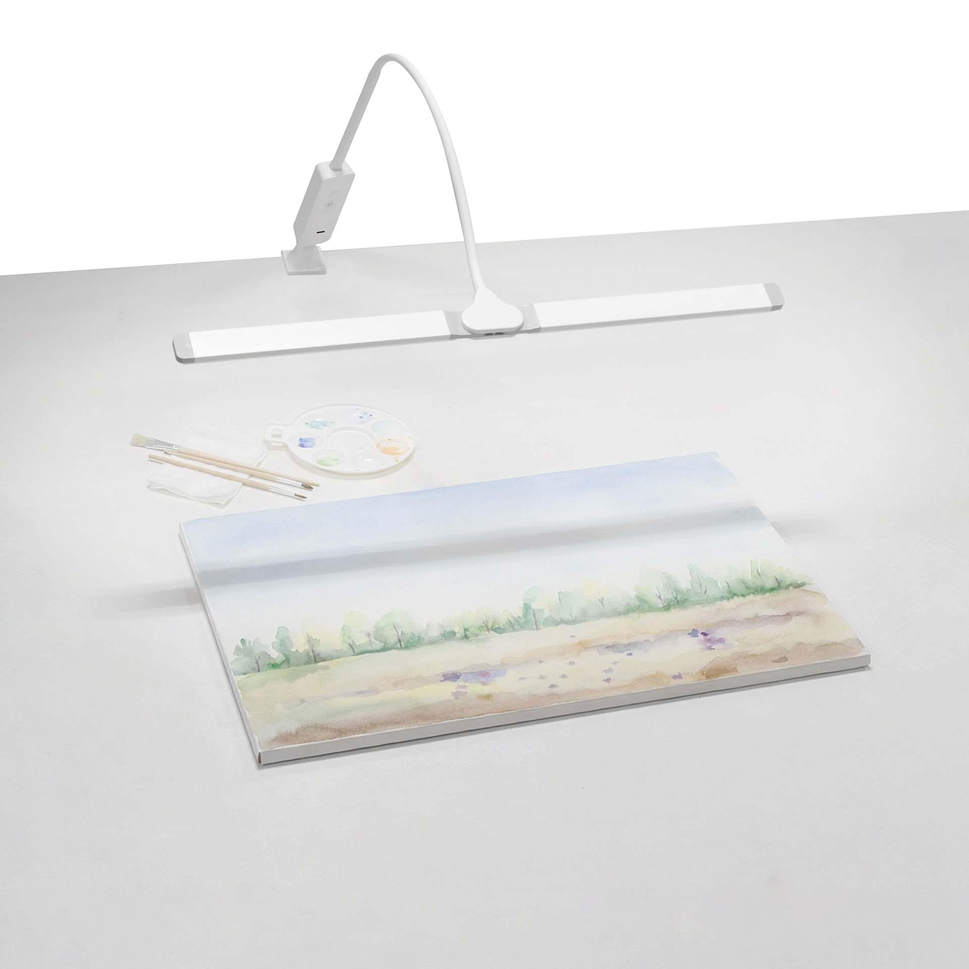 Artograph Split Bar Lamp with Table Clamp - White, on a desk with artwork