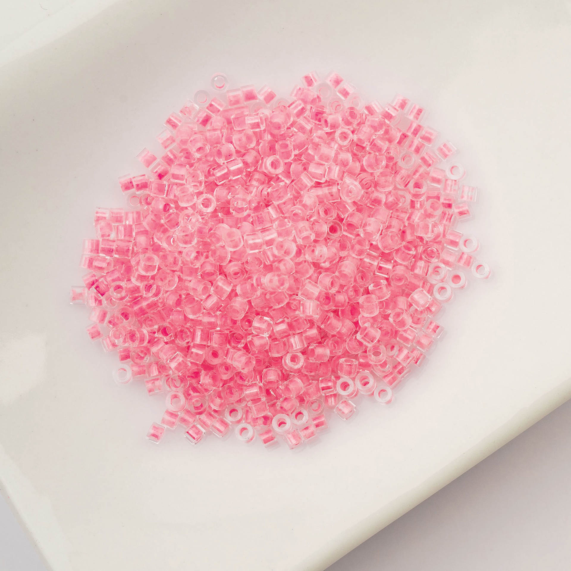 John Bead Cylin 11/0 Glow in the Dark Cylindrical Seed Beads - Rose, 25g sitting in dish