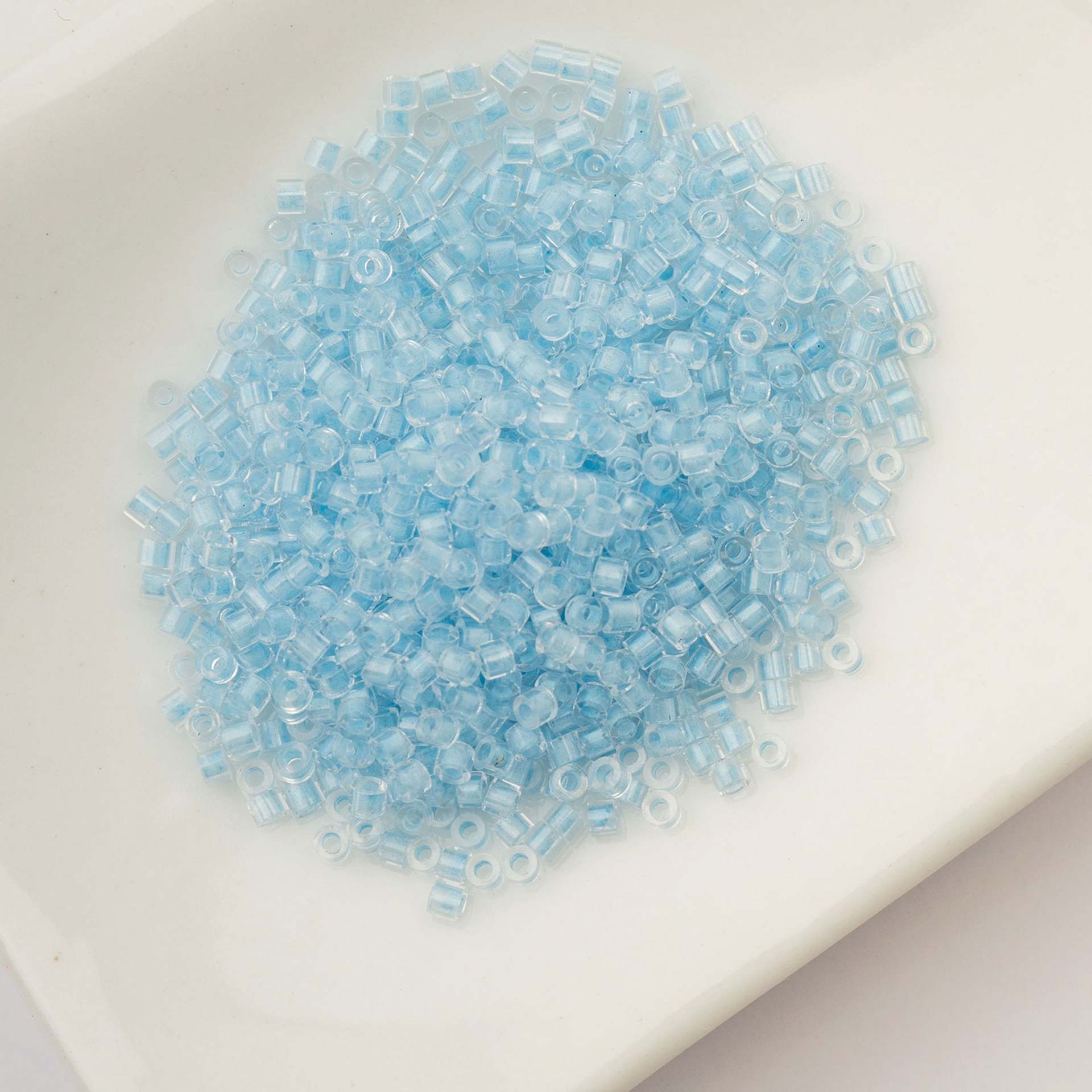 John Bead Cylin 11/0 Glow in the Dark Cylindrical Seed Beads - Blue, 25g sitting in dish