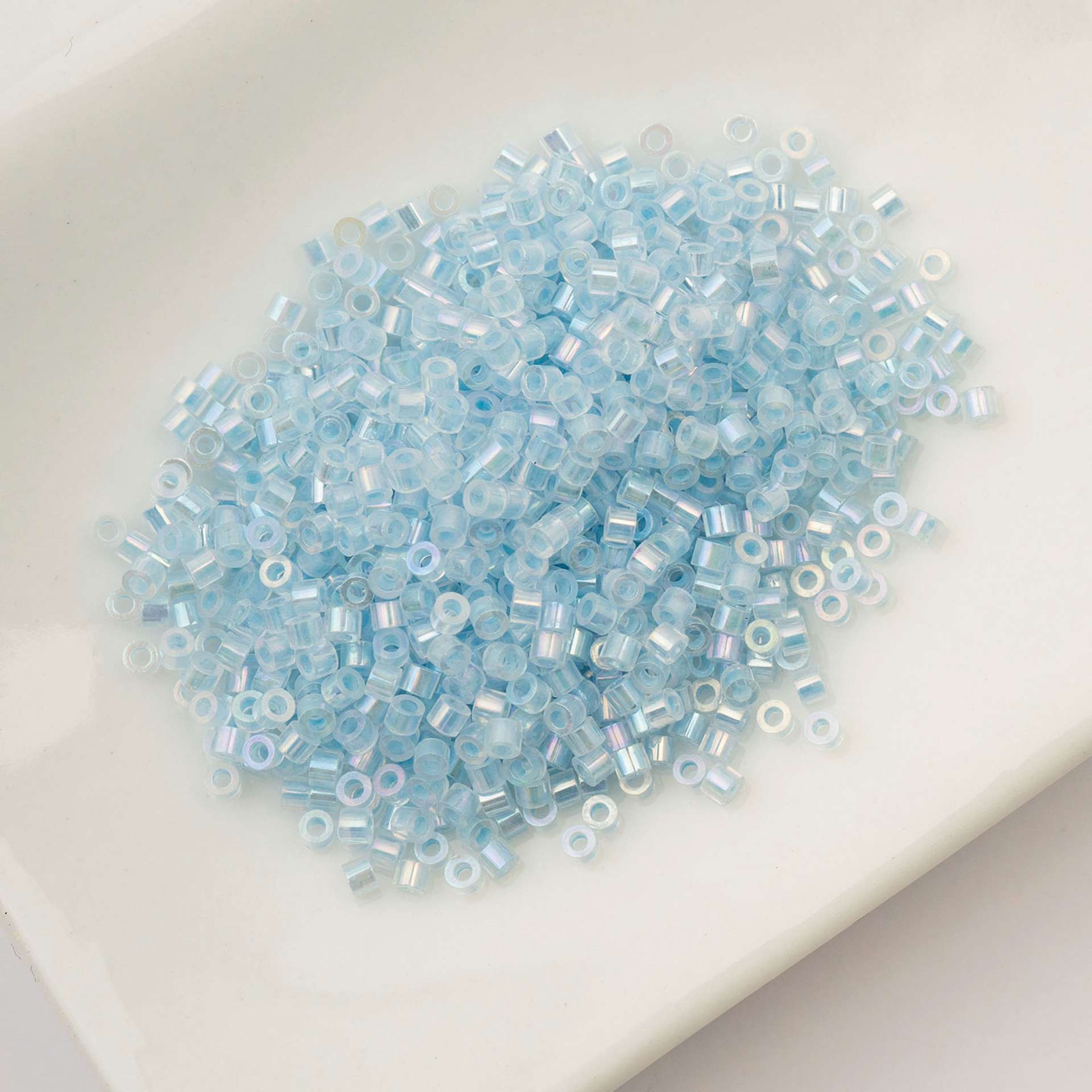 John Bead Cylin 11/0 Glow in the Dark Cylindrical Seed Beads - Blue AB, 25g sitting in dish