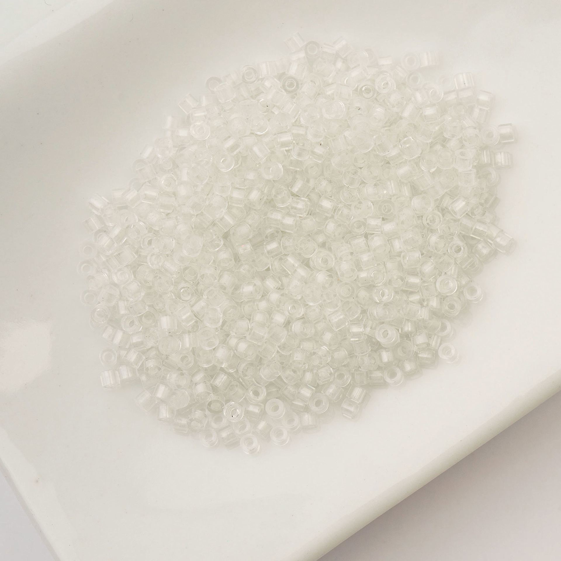 John Bead Cylin 11/0 Glow in the Dark Cylindrical Seed Beads - White to Sky, 25g sitting in dish