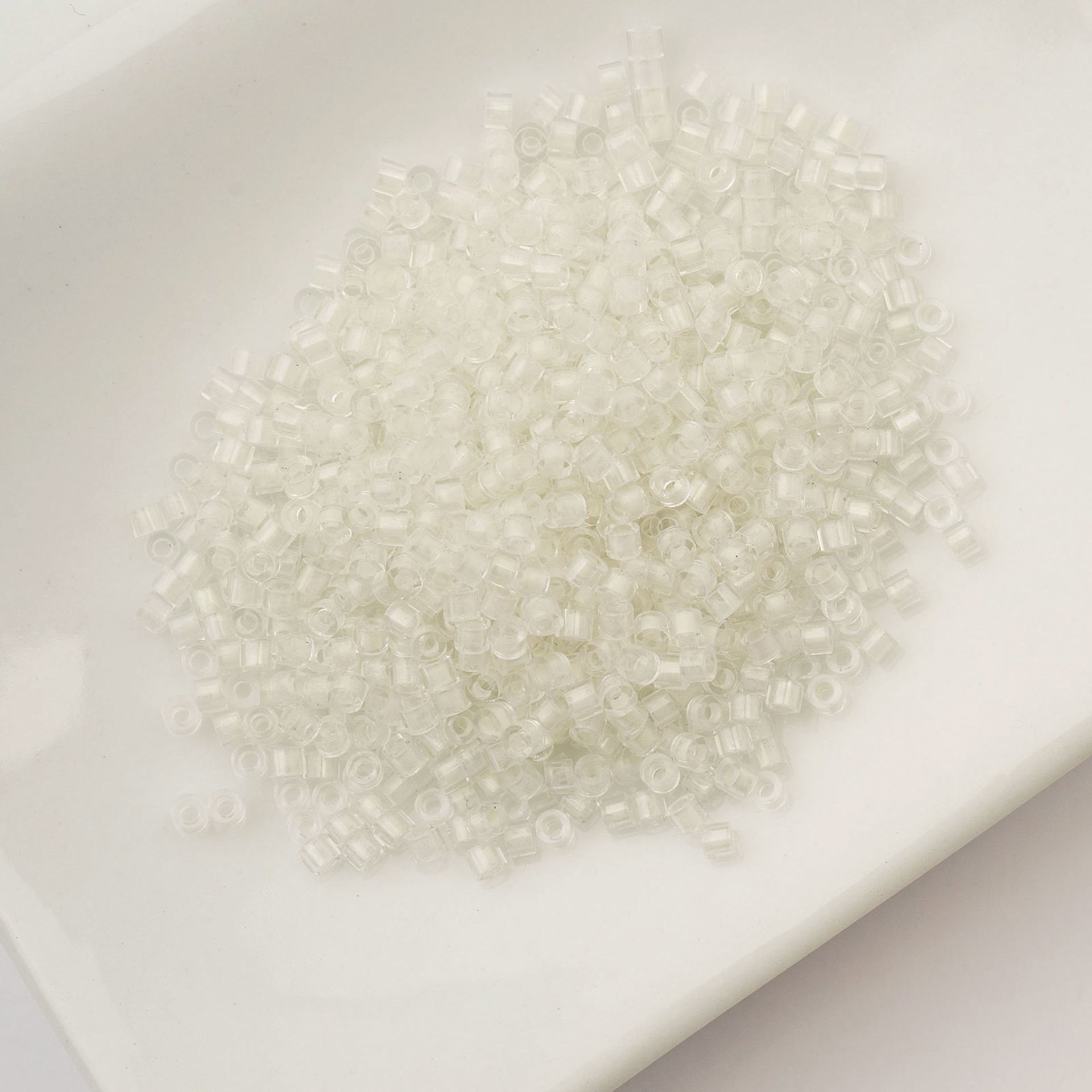 John Bead Cylin 11/0 Glow in the Dark Cylindrical Seed Beads - White to Green, 25g sitting in dish