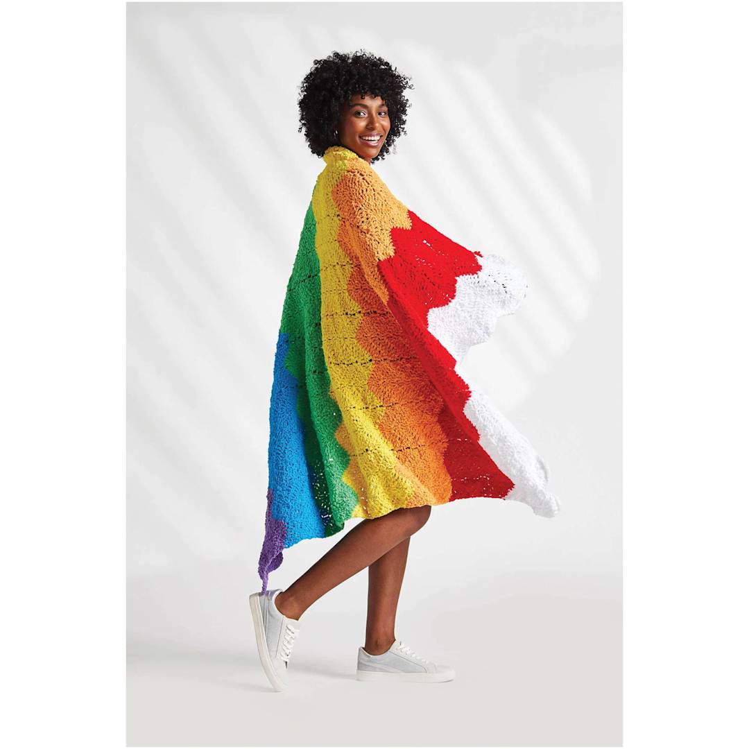 Open in modal - Premier Yarn Pixie Dust Brights Yarn, adult wearing a multicolor throw blanket made of yarn