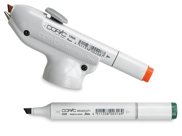 Open in modal - Copic Air Grip with Orange Copic marker loaded, and Green Copic marker nearby (Markers not Included)