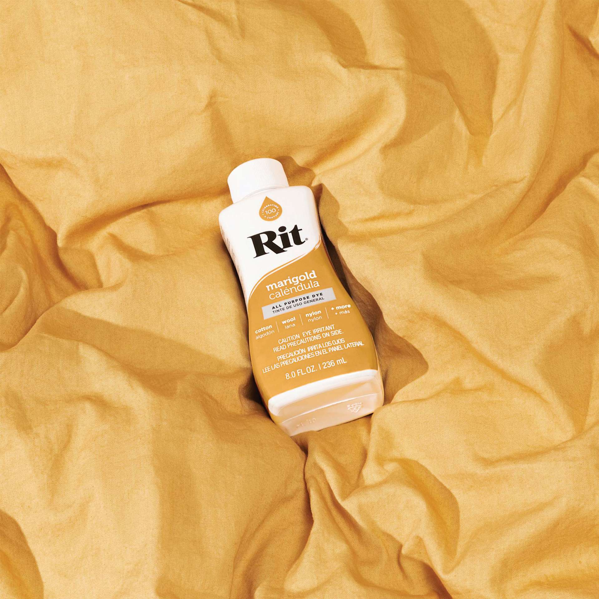 Rit All Purpose Liquid Dye - Marigold, 8 oz bottle on top of dyed fabric