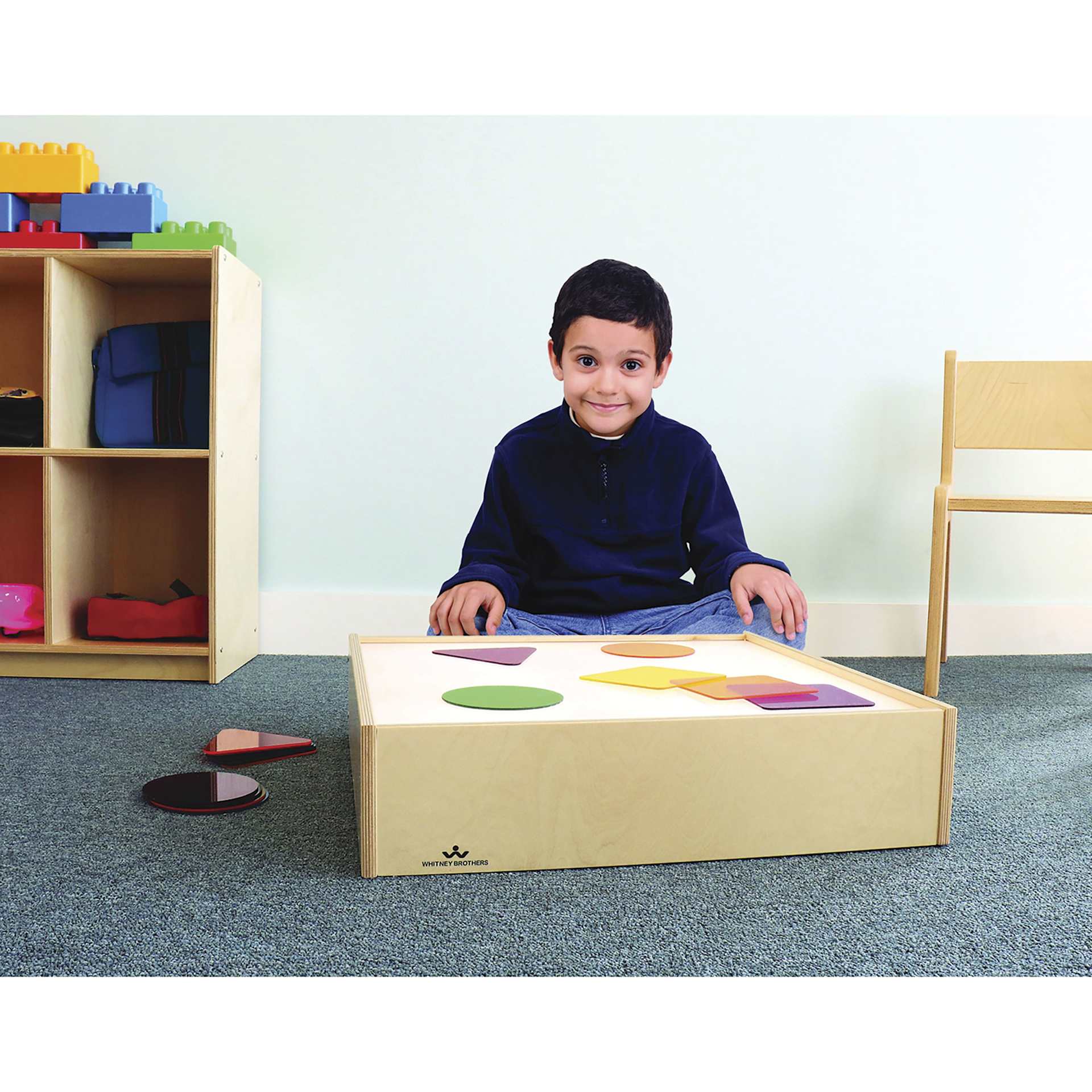 Whitney Brothers Tabletop Light Box, child seated next to the box and shapes on the box