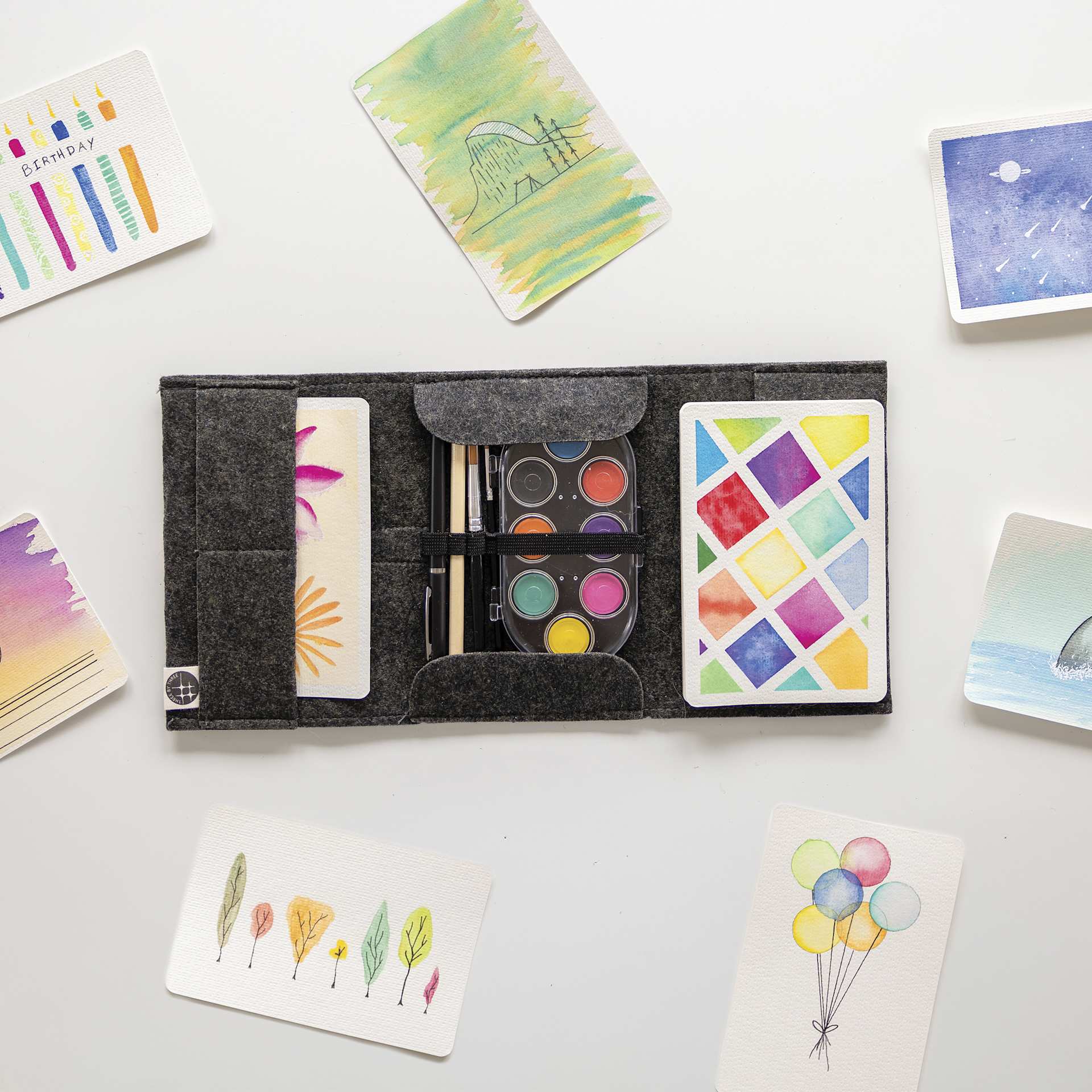 Three By Three Jotblock Travel Postcard Watercolor Paint Set, on table with finished art pieces