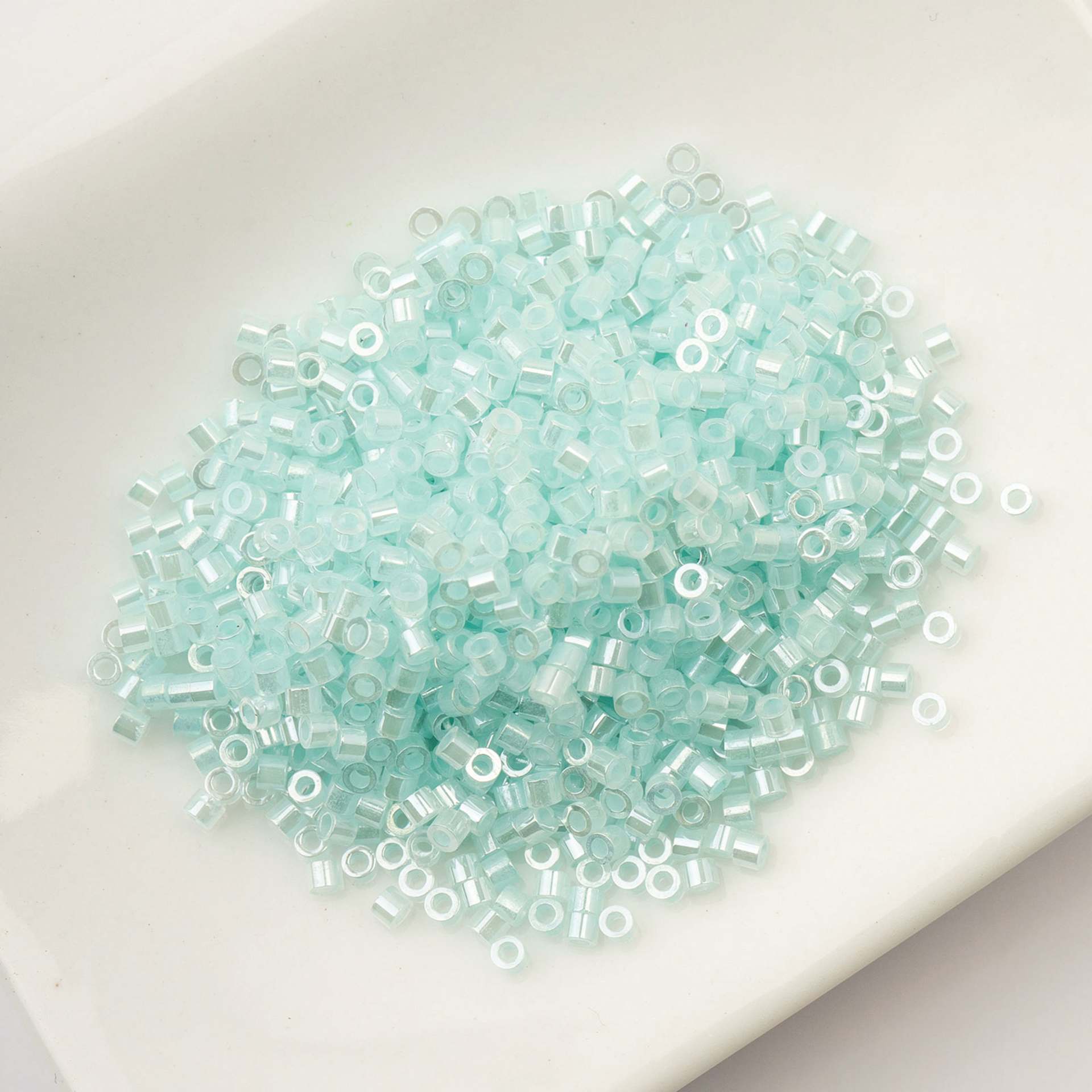 John Bead Cylin 11/0 Ceylon Cylindrical Seed Beads - Light Crystal Aqua, 25g sitting in dish