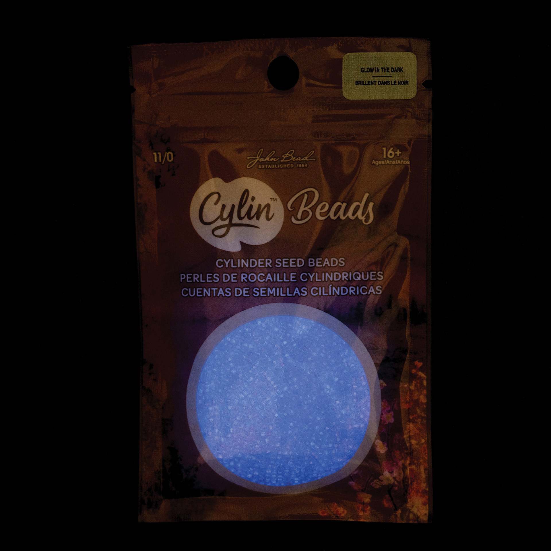 John Bead Cylin 11/0 Glow in the Dark Cylindrical Seed Beads - Violet, 25g front of packaging to show glow effect