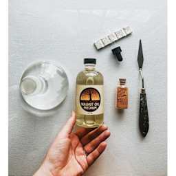 Natural Earth Paint Refined Walnut Oil - held beside a bottle of pigment, water, and a palette knife
