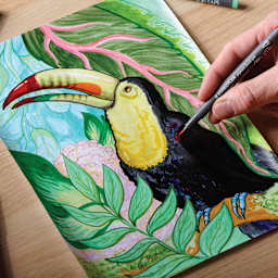 Staedtler Pigment Arts Pen in hand coloring a drawing of a tucan