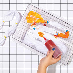 Rit All Purpose Liquid Dye - Sunshine Orange, 8 oz, hand holding squirt bottle tie dyeing fabric