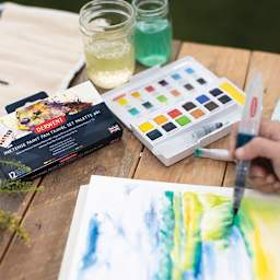 Derwent Inktense Paint Pan Set -Artist painting with Derwent Inktense Paint palette adjacent
