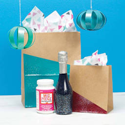Plaid Mod Podge Sparkle Finish, jar next to painted and finished gift bags and bottle with Sparkle