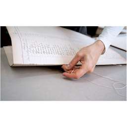 Closeup of hand using Lineco Binder's Needle to bind Ledger pages together