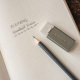 Blackwing Handheld Eraser with Grey Holder, on top of paper next to pencil (not included)