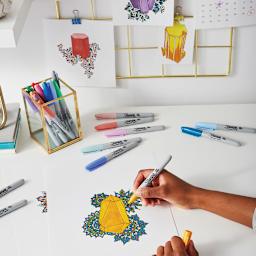 Sharpie Fine Point Permanent Markers spread out on a table and one held in hand making art
