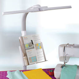OttLite Dual Shade LED Floor Lamp - shown with Book illuminated on stand at a sewing station