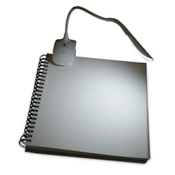 Daylight Smart Clip-On Lamp clipped on top of sketchbook in dark space