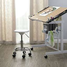 Studio Designs Studio Stool, in front of a drafting table stationed in a room