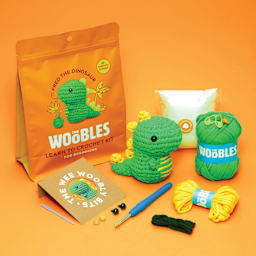 The Woobles Beginner Crochet Amigurumi Kit - Dinosaur, finihsed design and contents laid out in front of packaging