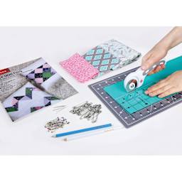 Singer Learn to Quilt Starter Kit, cutter in hand slicing fabric on cutting mat