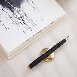 Tom's Studio Solid Brass Pen Rest - Gold, with uncapped pen on a table (not included)