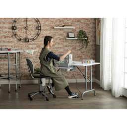 Studio Designs Folding Sewing Table, seated seamstress using sewing machine (not included) on table