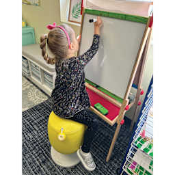 Child using a yellow Kore Design Kid’s Adjustable Pivot Stool at an easel.
