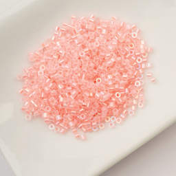 John Bead Cylin 11/0 Glow in the Dark Cylindrical Seed Beads - Coral AB, 25g sitting in dish