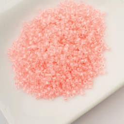 John Bead Cylin 11/0 Glow in the Dark Cylindrical Seed Beads - Coral, 25g sitting in dish