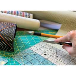 Olfa Stainless-Steel Snap-Off Graphics Knife, in hand cutting paper with a ruler