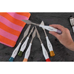 Gamblin Palette Knives (a hand holding The Hoyt knife, the other versions laying on the table)