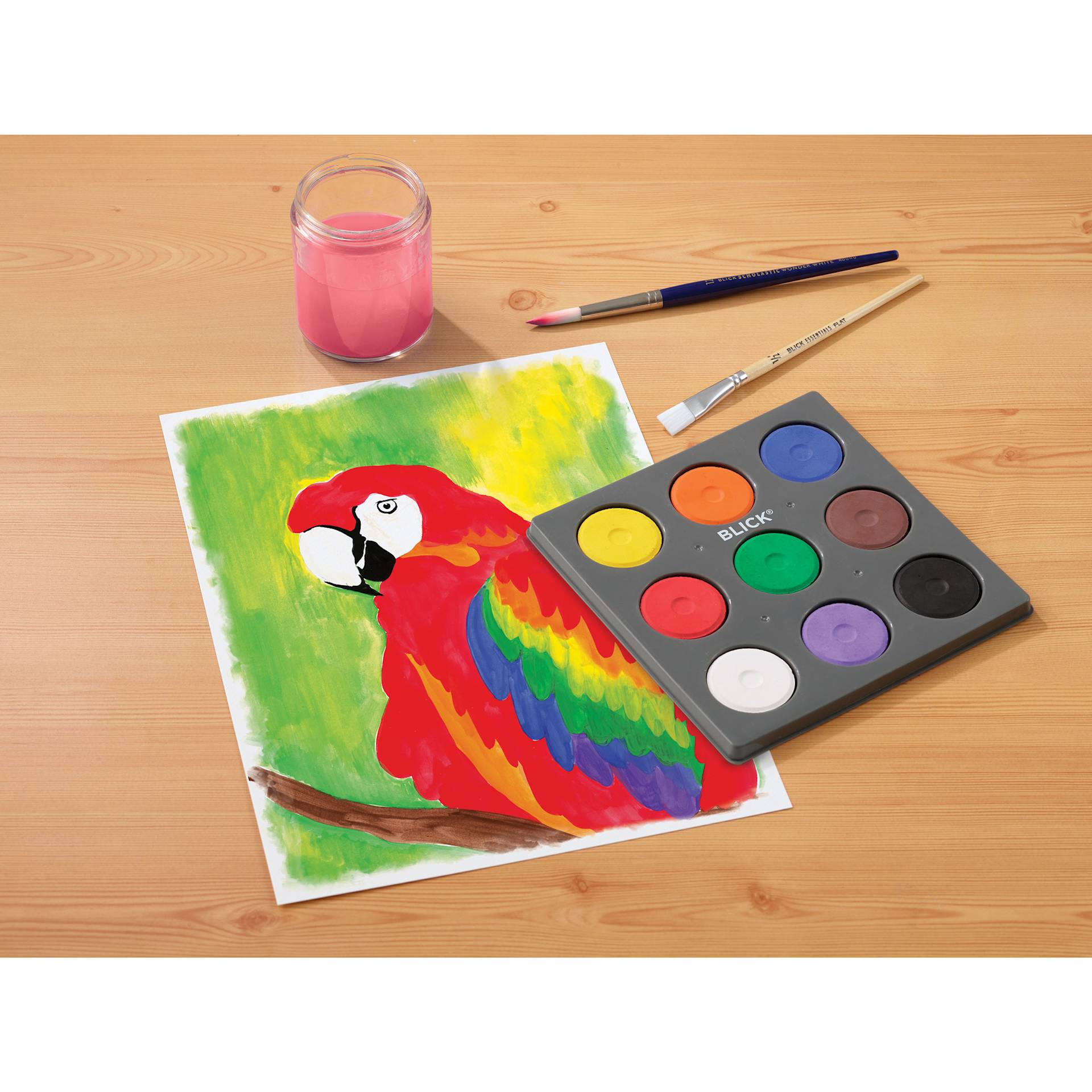 Blick Essentials Tempera Cakes Set of 9 Classic Colors in a tray, with brushes, a water cup, and a painting of a parrot.