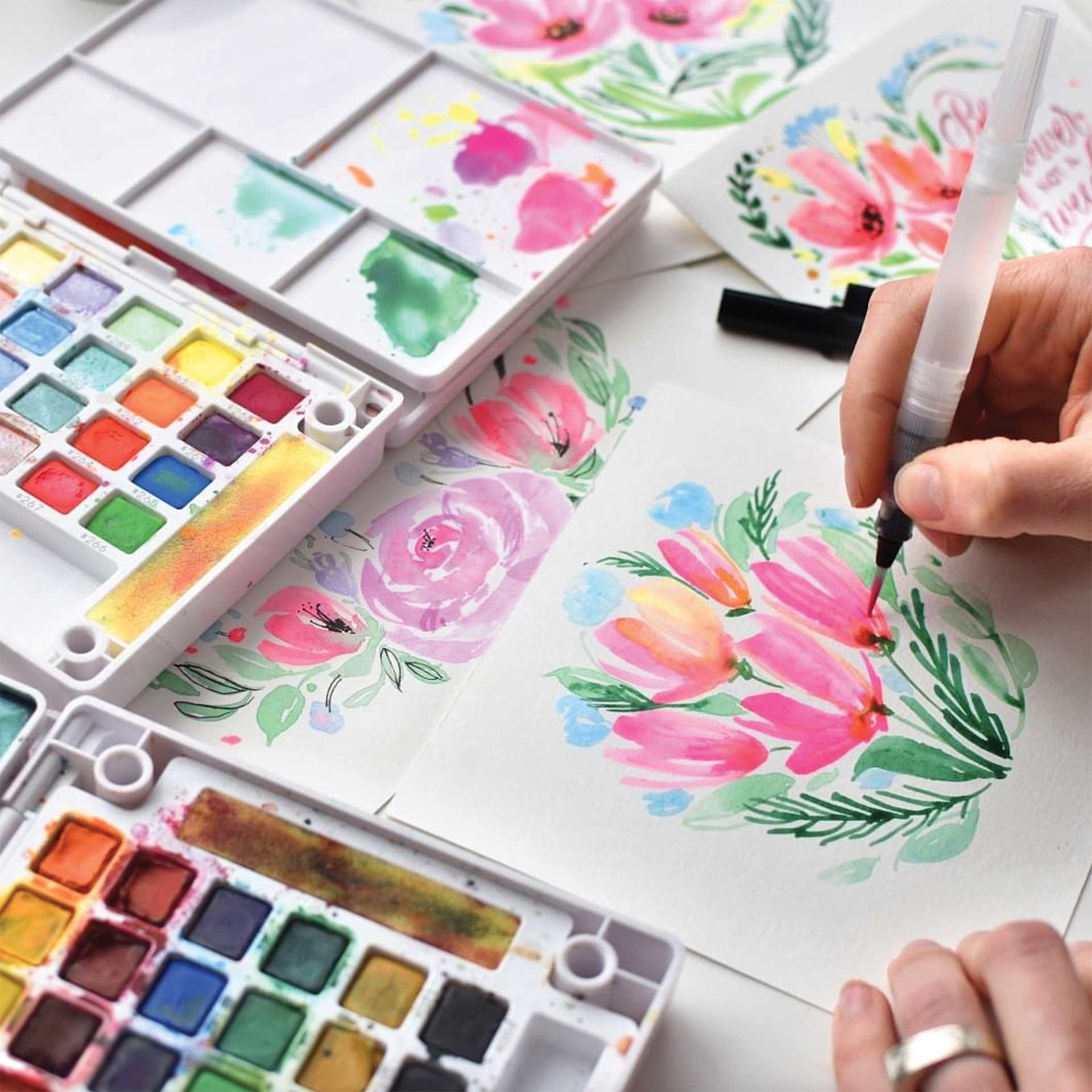 Sakura Koi Watercolor Half Pan - Set of 48 Sketch Box, Assorted Colors open sets beside painting of flowers