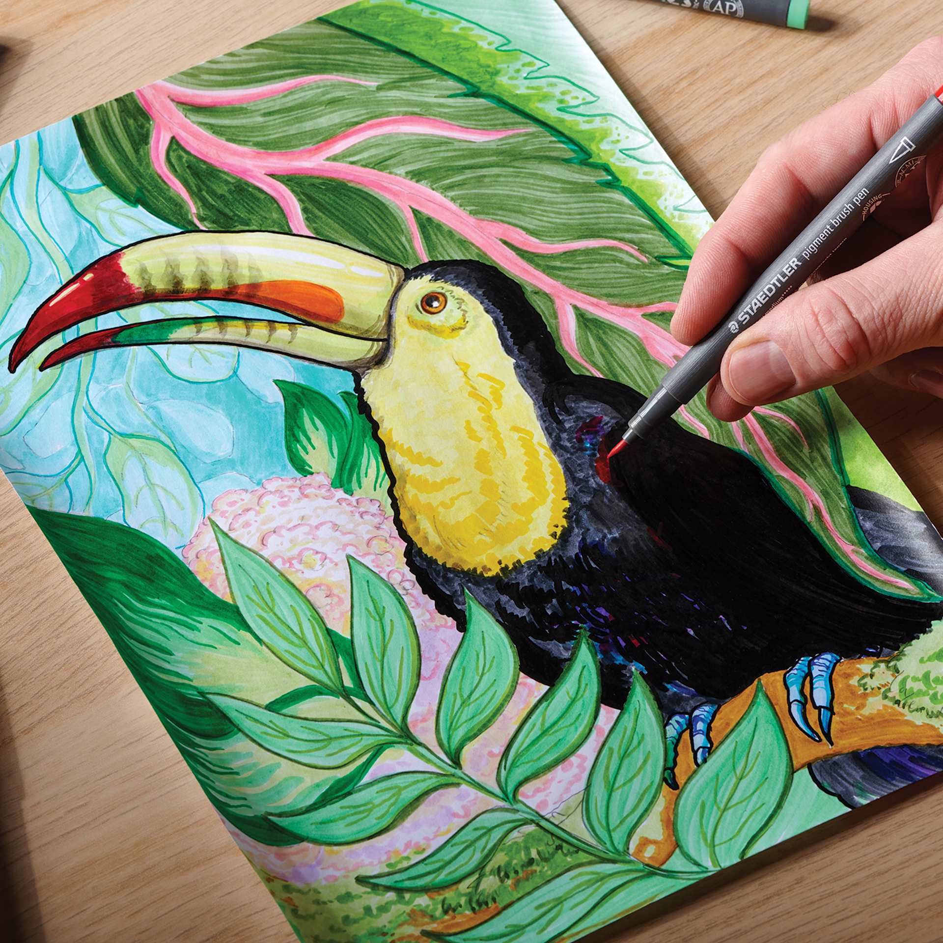 Staedtler Pigment Arts Pen in hand coloring a drawing of a tucan Staedtler Pigment Arts Pen in hand coloring a drawing of a tucan