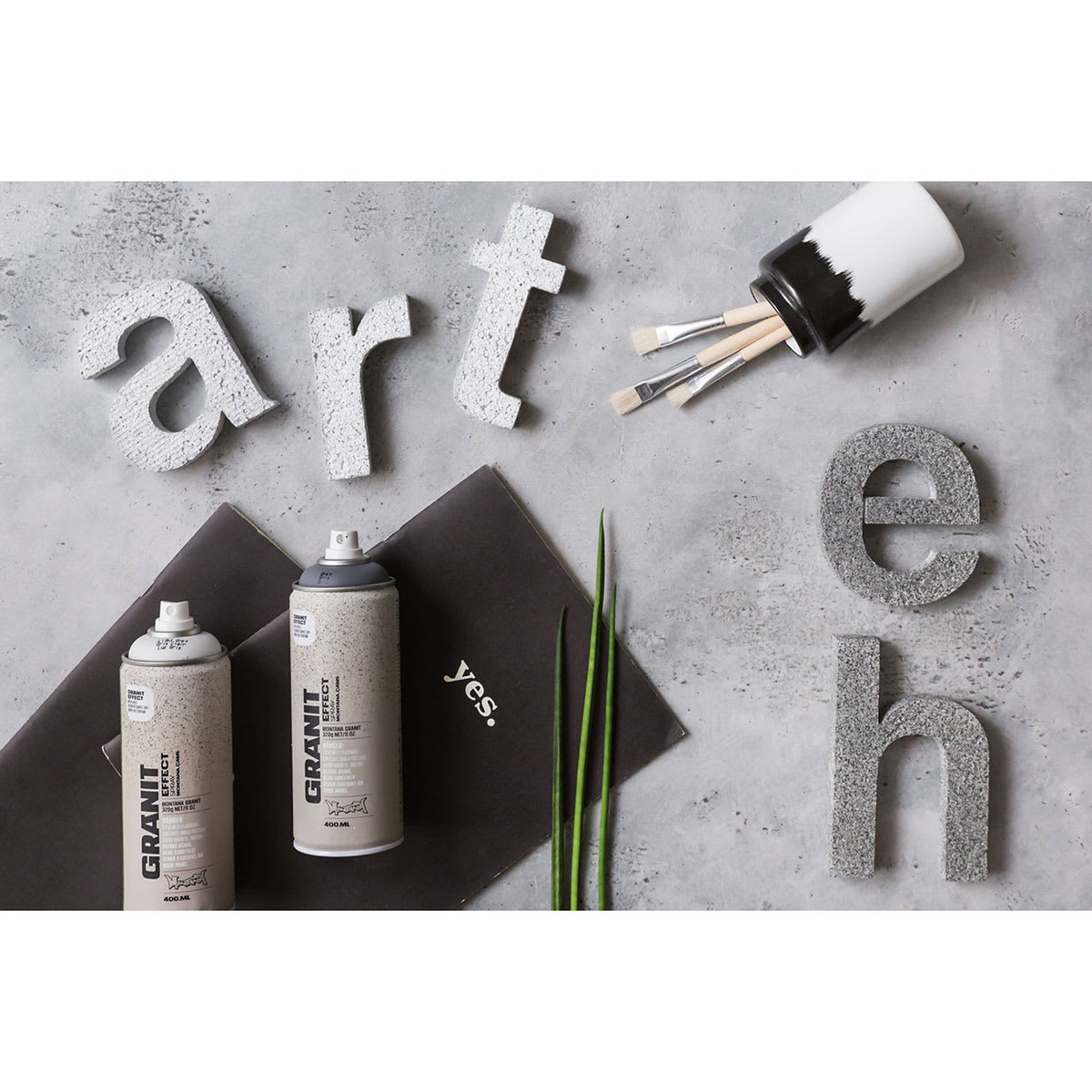 Montana Granit Effect Spray - 2 cans laying on desk with several painted 3D letters Montana Granit Effect Spray - 2 cans laying on desk with several painted 3D letters