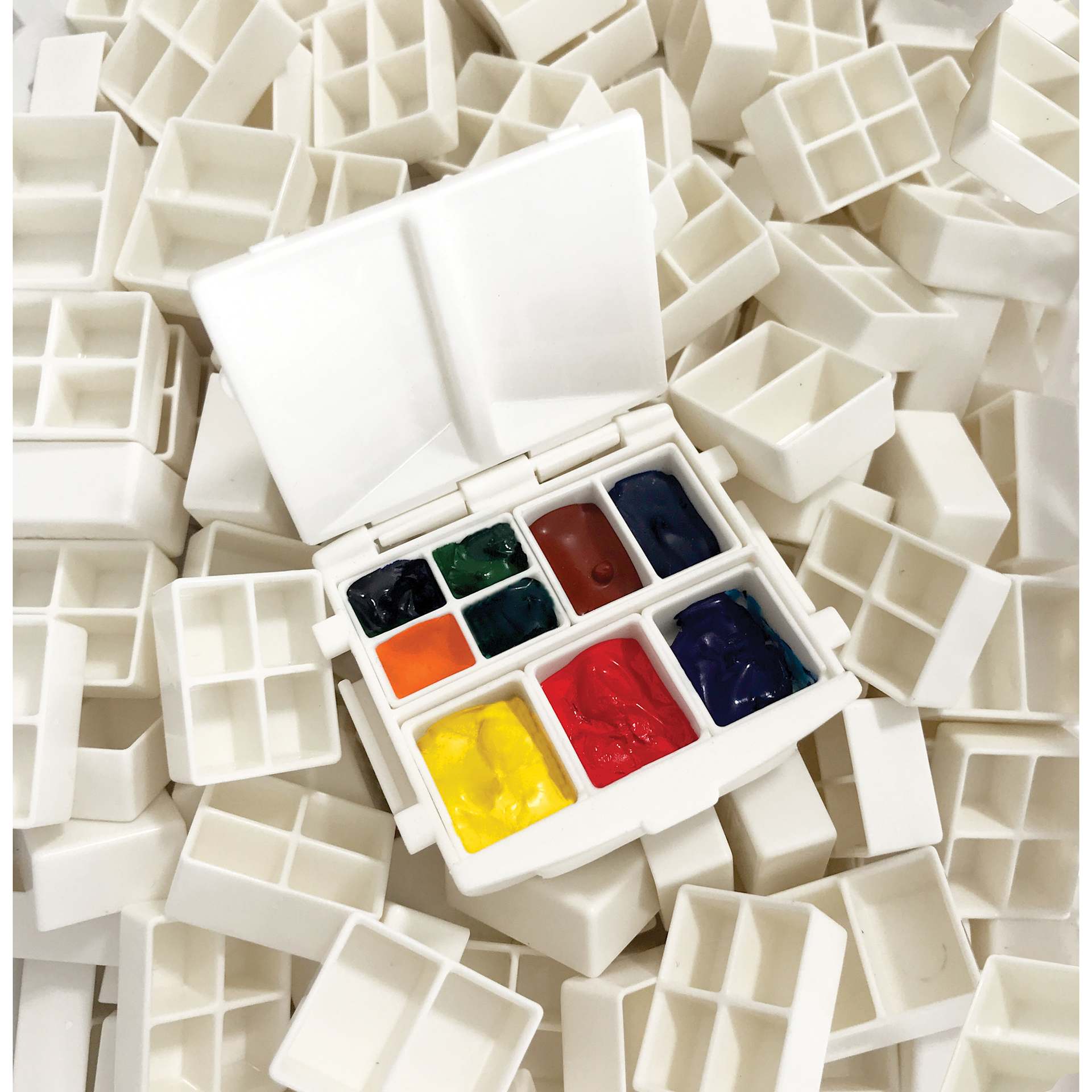 A filled Portable Painter Micro Watercolor Palette sitting on a variety of other pans.