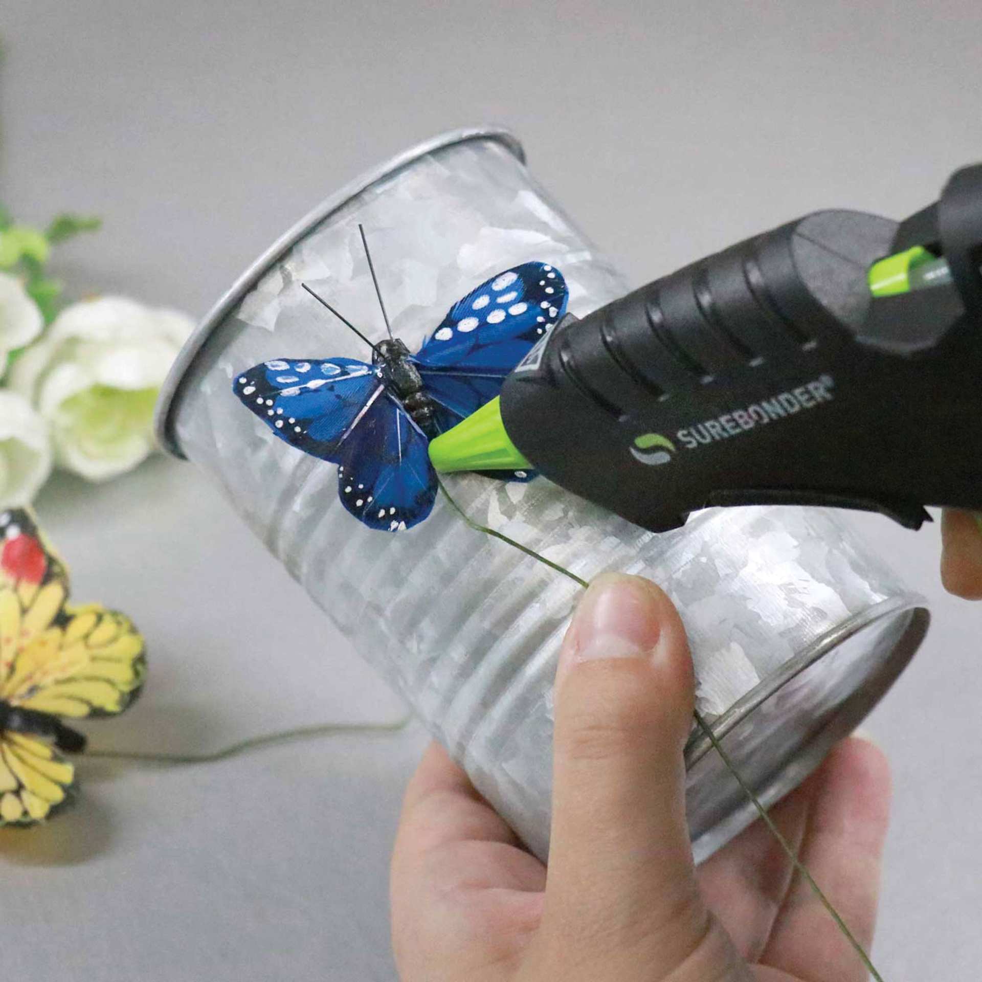 Surebonder Plus Series Mini Dual Temp Glue Gun, in hand being used to glue a design to a can Surebonder Plus Series Mini Dual Temp Glue Gun, in hand being used to glue a design to a can