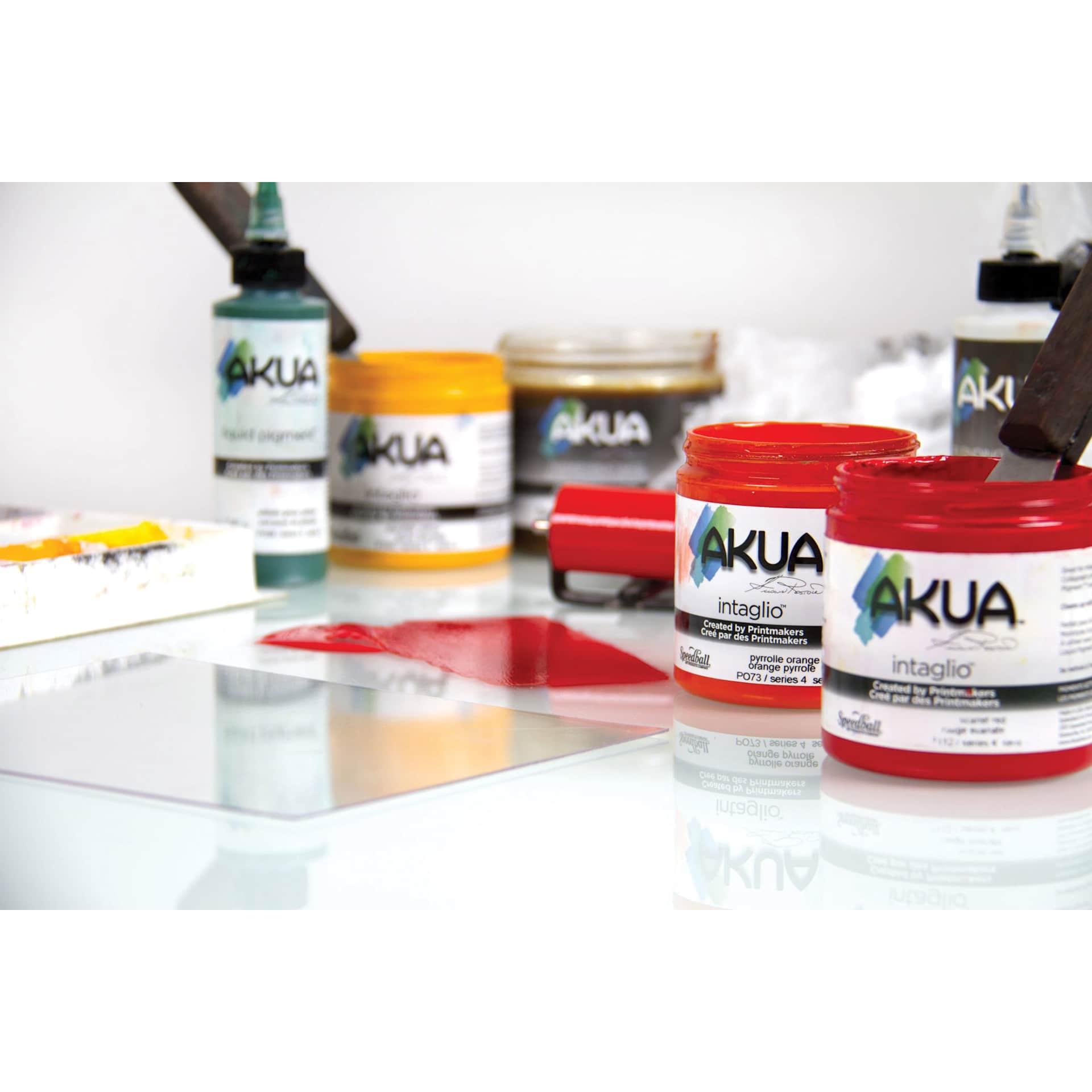 Akua Intaglio Inks jars of various colors grouped together beside rubber brayer